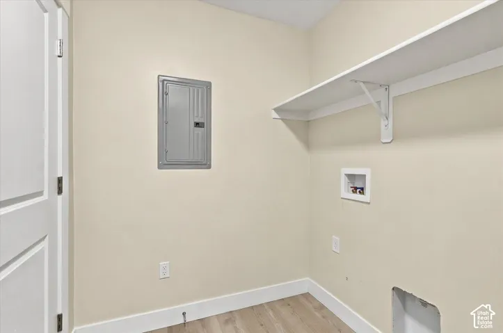 Utility area featuring wood-finish flooring, a wall-mounted electrical panel, a built-in wall shelf with support brackets, and recessed plumbing connections