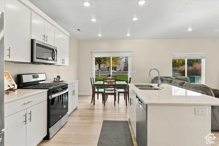 Kitchen featuring white shaker-style cabinetry, quartz countertops, a central island with a double-basin undermount sink, stainless steel appliances, and wood-finish flooring