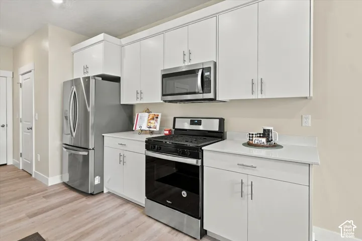 Kitchen featuring white cabinetry, quartz countertops, stainless steel appliances, and wood-finish flooring