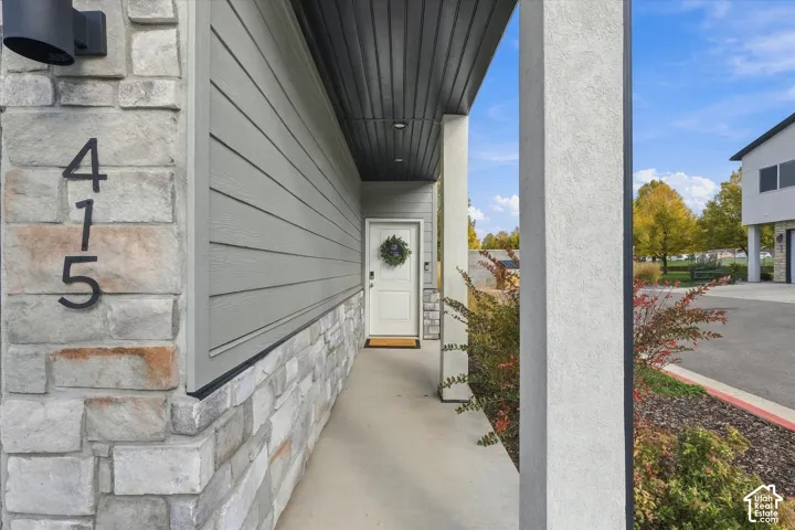 Covered entryway featuring natural stone veneer siding, horizontal lap siding, a smooth concrete porch, and a dark metallic porch ceiling