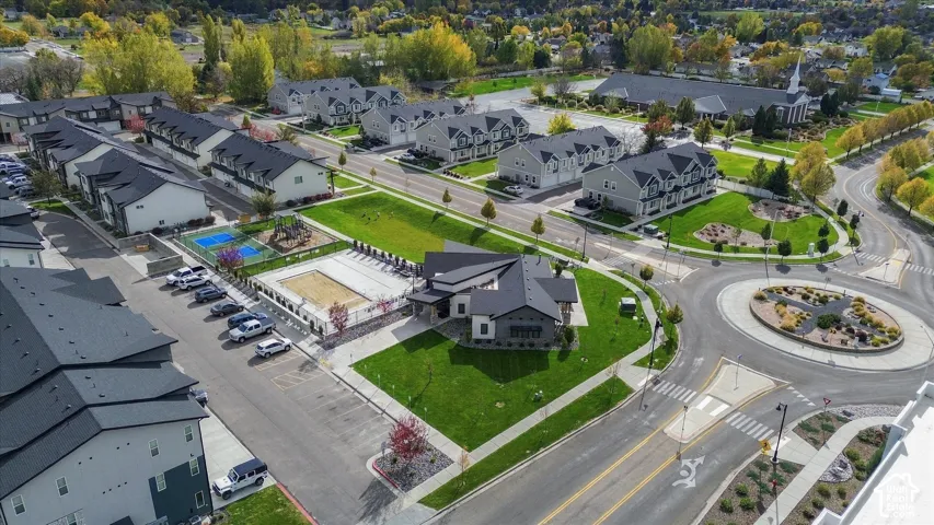 Aerial perspective featuring a multi-unit residential community with a swimming pool, fenced sport court, designated surface parking, and landscaped green spaces