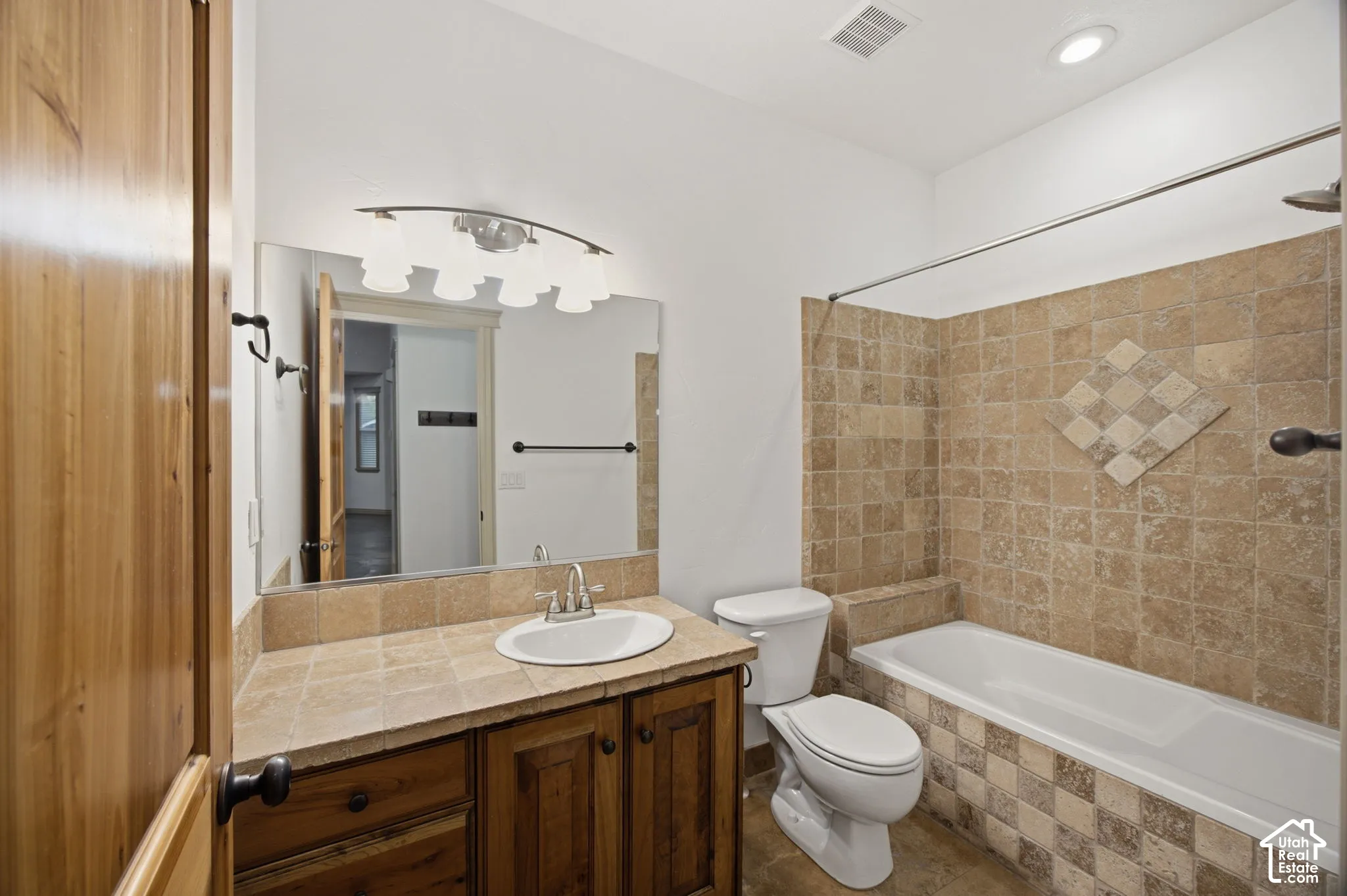 Bathroom featuring a vanity with a tile countertop, integrated basin, and natural wood cabinetry