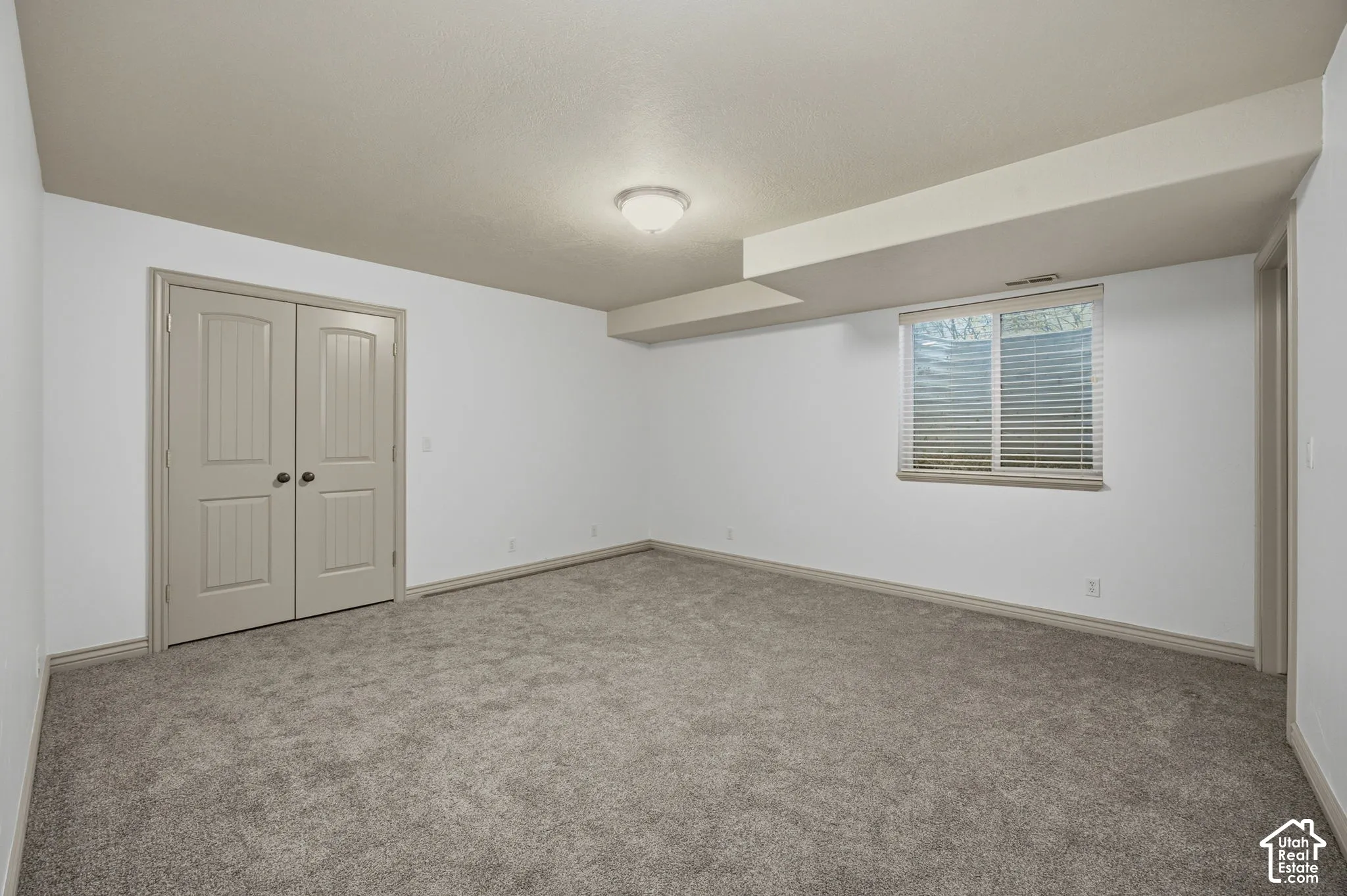 Neutral-toned room featuring wall-to-wall carpeting, double-panel interior doors, and a window with horizontal blinds