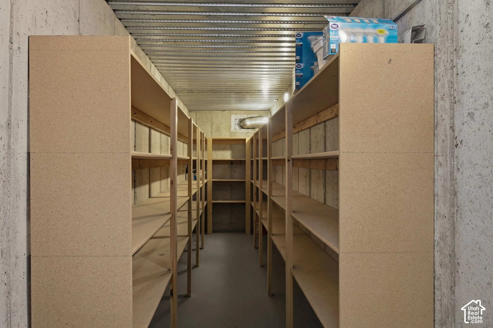 Storage room featuring built-in wood-composite shelving, exposed concrete walls, and corrugated metal ceiling paneling
