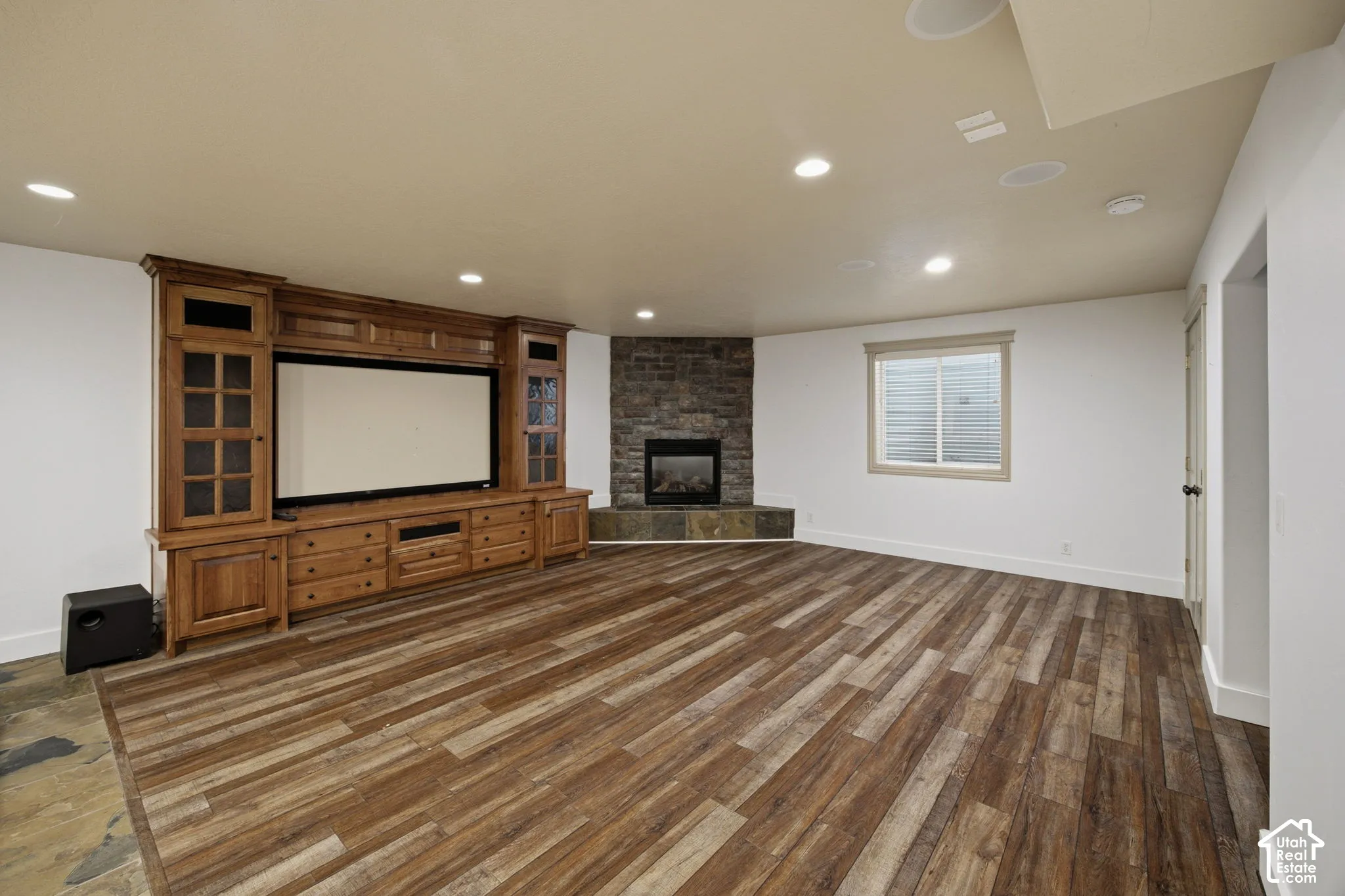 Custom built-in wood cabinetry, corner stone-veneer fireplace with hearth, recessed ceiling lighting, and wood-finish flooring