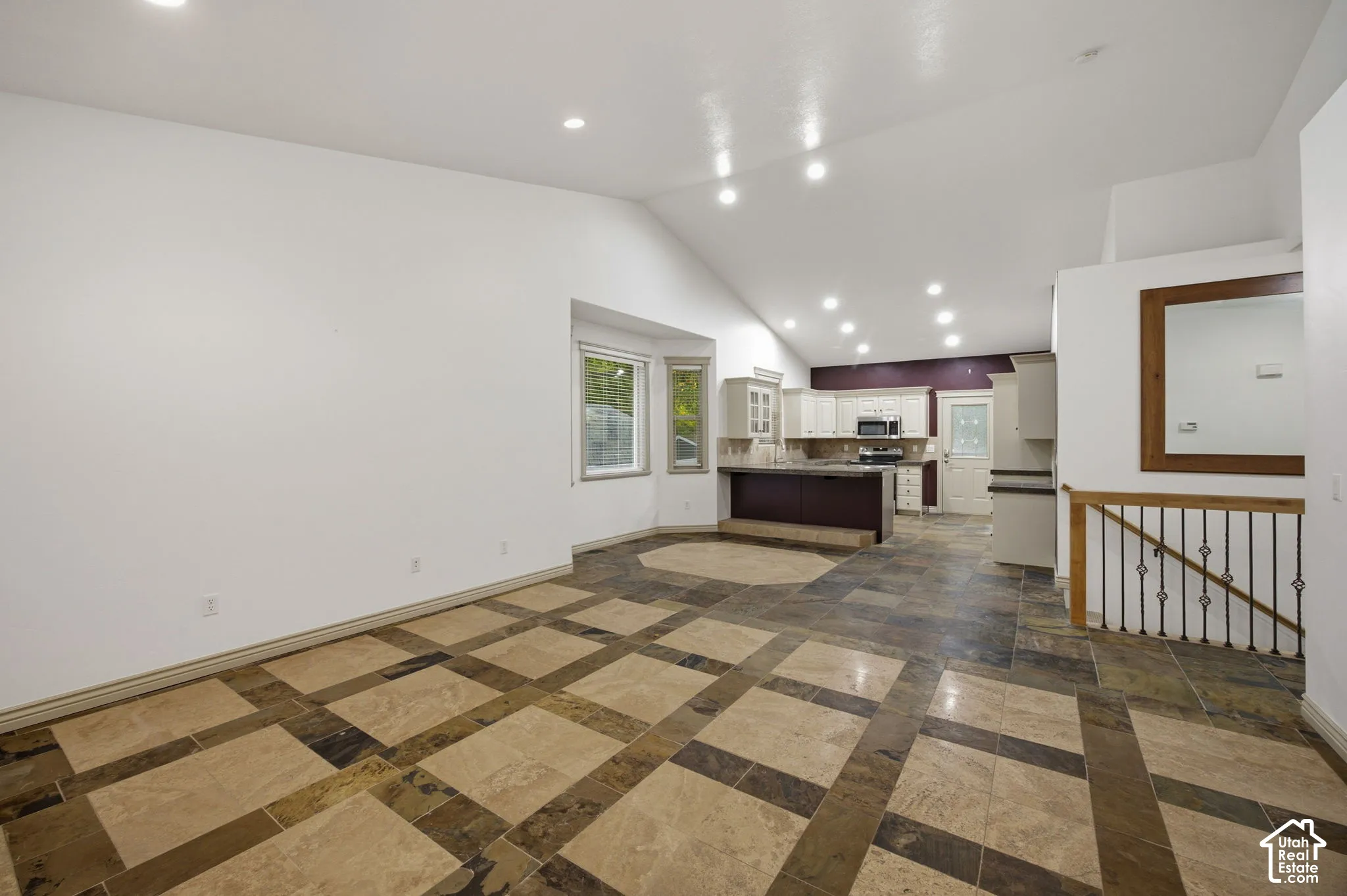 Vaulted ceilings with recessed lighting, tile flooring with decorative inlay patterns, breakfast bar, multi-pane window bay, and metal railing staircase detail