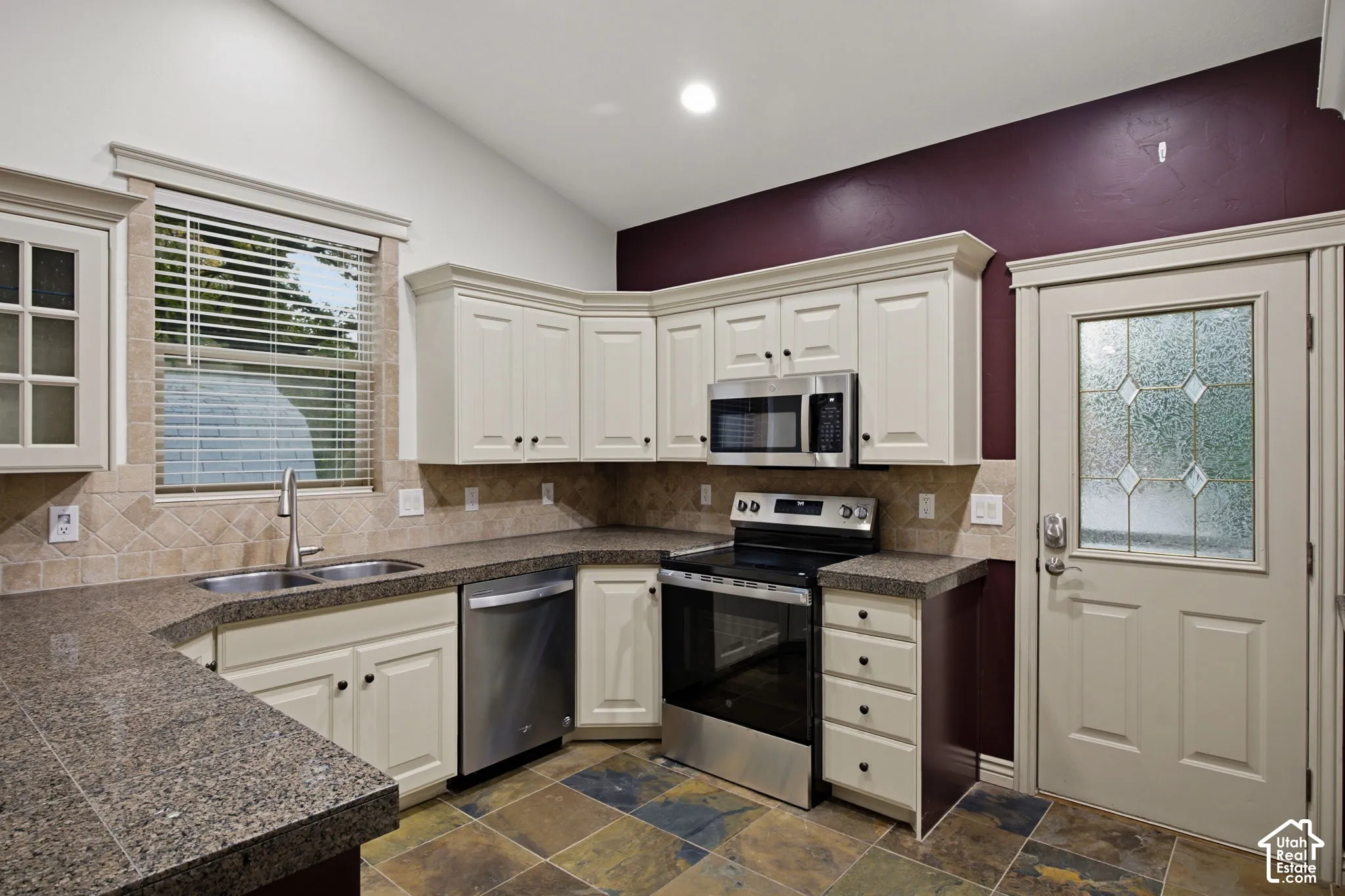 Kitchen featuring off-white cabinetry, stone-finish countertops, stainless steel appliances, multi-colored tile flooring, and a glass-paneled exterior door
