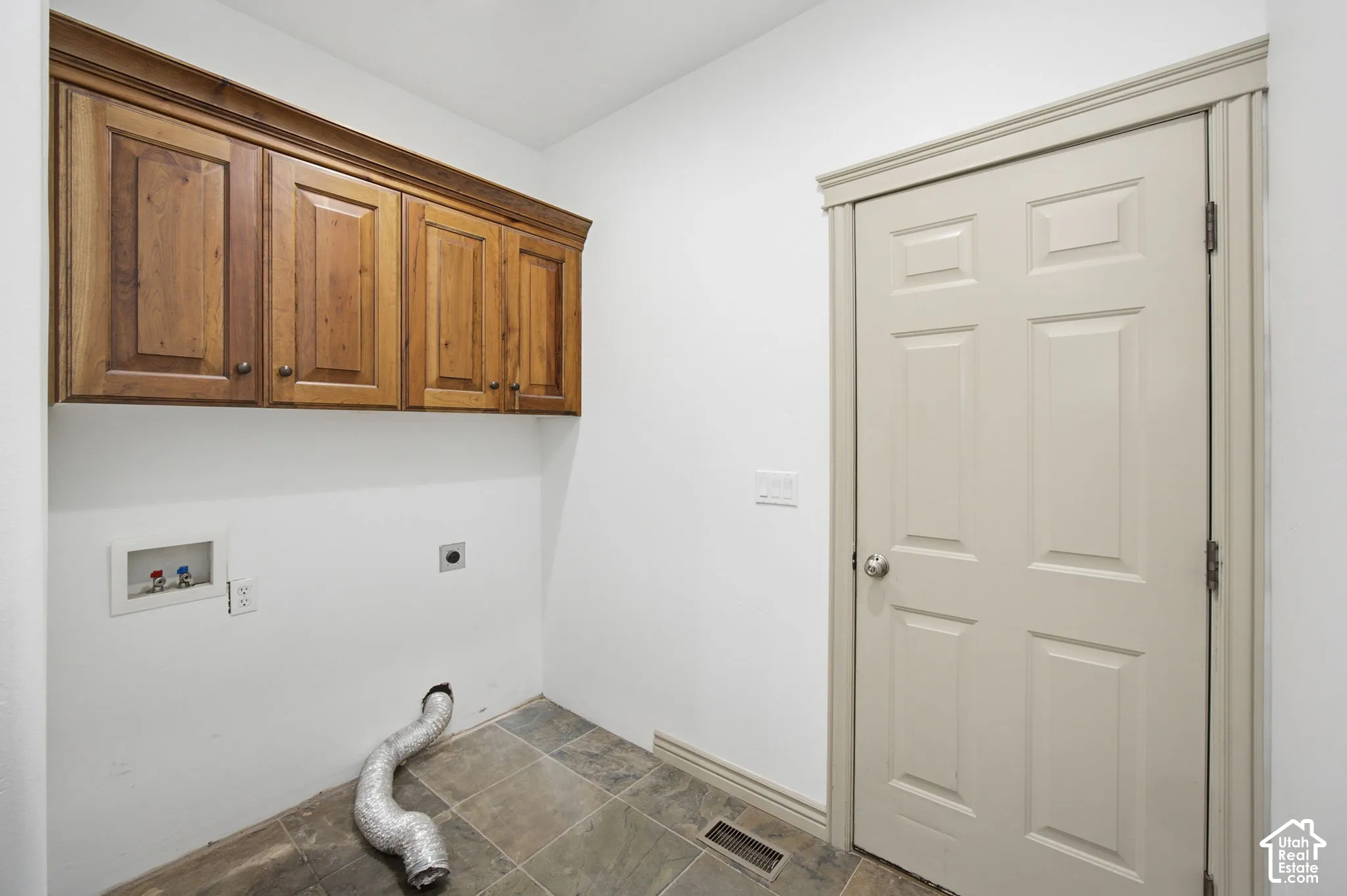 Utility area featuring wood-finish wall-mounted cabinetry, tile flooring, and a six-panel interior door