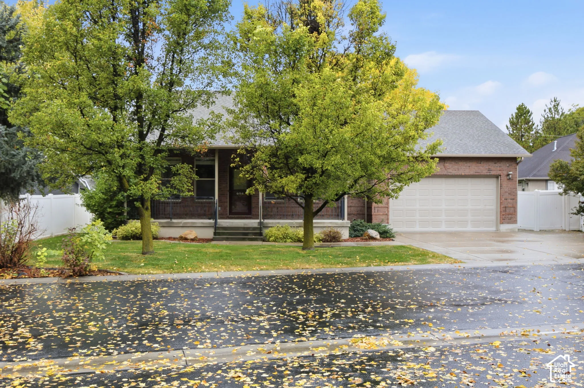 Brick exterior residence featuring a covered front porch, an attached garage, and mature trees