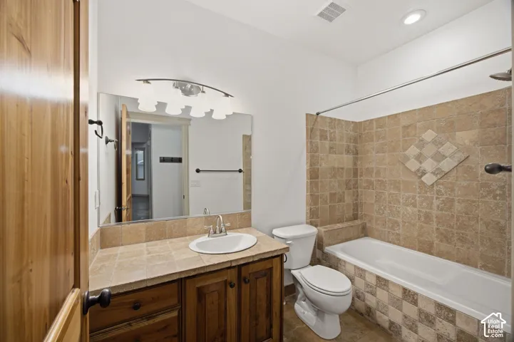 Bathroom featuring a vanity with a tile countertop, integrated basin, and natural wood cabinetry