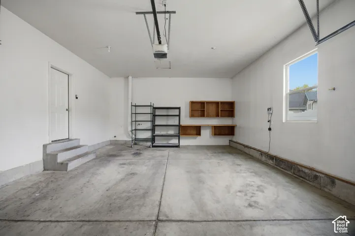 Garage interior featuring concrete flooring, wall-mounted wood cabinetry, a dedicated exterior access door with concrete steps, and an integrated garage door opener