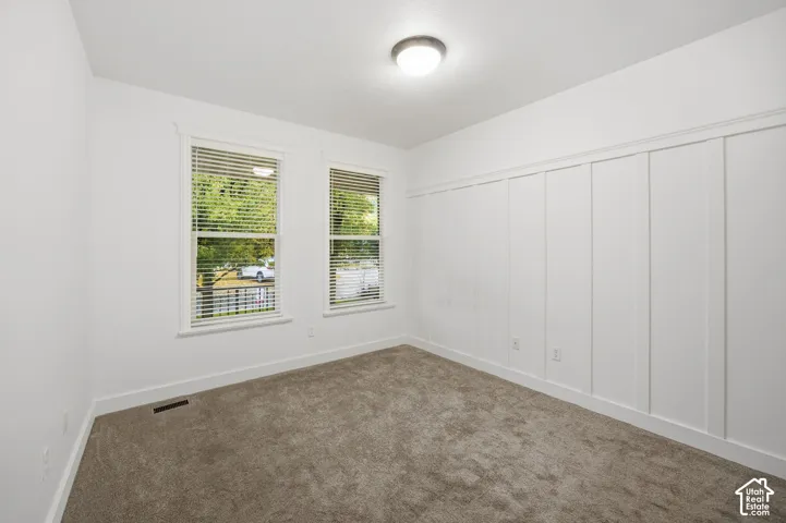 Interior room featuring vertical board-and-batten wall detailing, neutral carpeting, dual windows with installed blinds, and a central flush-mount ceiling light fixture