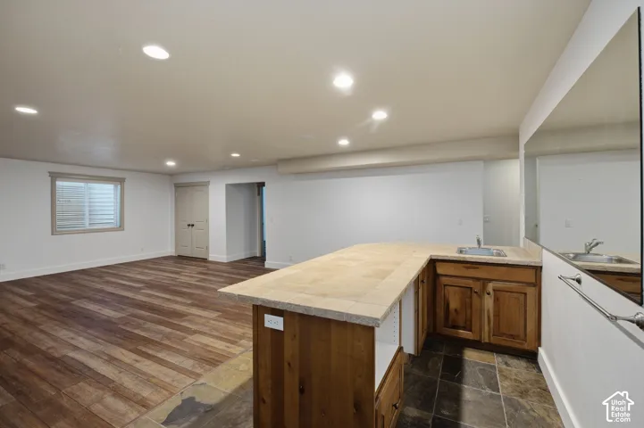 Open-concept area featuring wood-finish flooring, recessed lighting, and a kitchenette equipped with tile countertops, wood cabinetry, and a stainless steel sink