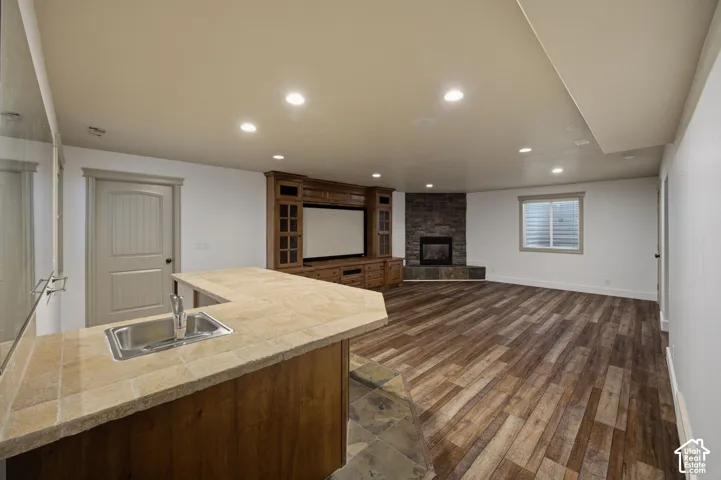 Built-in cabinetry with integrated media center, stone-surround fireplace, tile-topped wet bar with stainless steel sink, wood-finish flooring, and recessed lighting