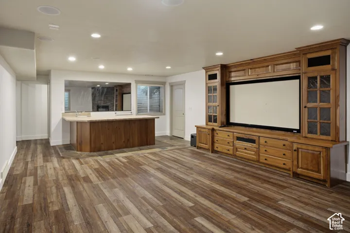 Wood-finish flooring, custom built-in cabinetry with integrated media center, wet bar with stone-surfaced countertop, and recessed ceiling lighting