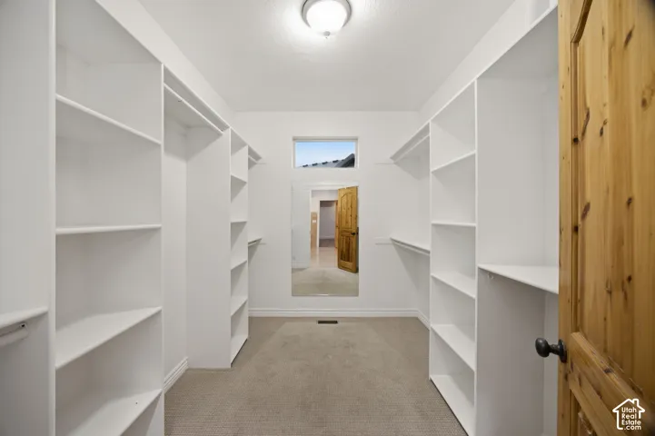 Walk-in closet featuring floor-to-ceiling white built-in shelving, carpeted flooring, a full-length wall-mounted mirror, and a transom window