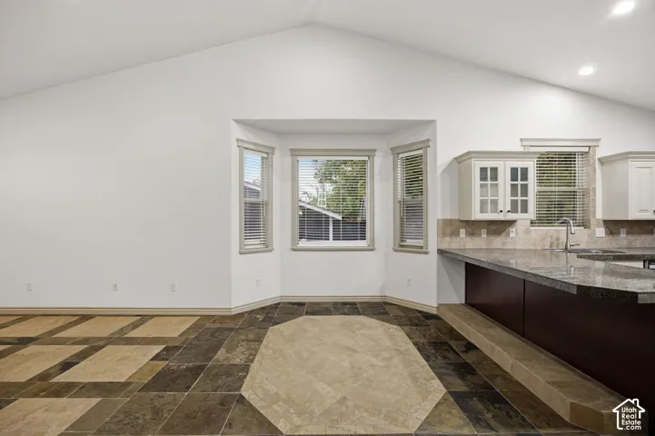 Vaulted ceilings, bay window, stone-patterned tile flooring, breakfast bar with stone countertop, and upper cabinetry with glass-panel doors