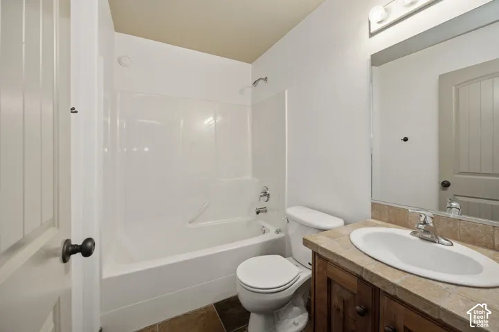 Bathroom featuring a tub and shower combination with a molded surround, vanity with tile-topped counter and oval undermount sink, and three-light wall fixture above a rectangular mirror