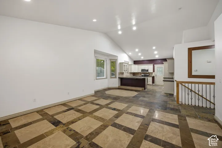 Vaulted ceilings with recessed lighting, tile flooring with decorative inlay patterns, breakfast bar, multi-pane window bay, and metal railing staircase detail