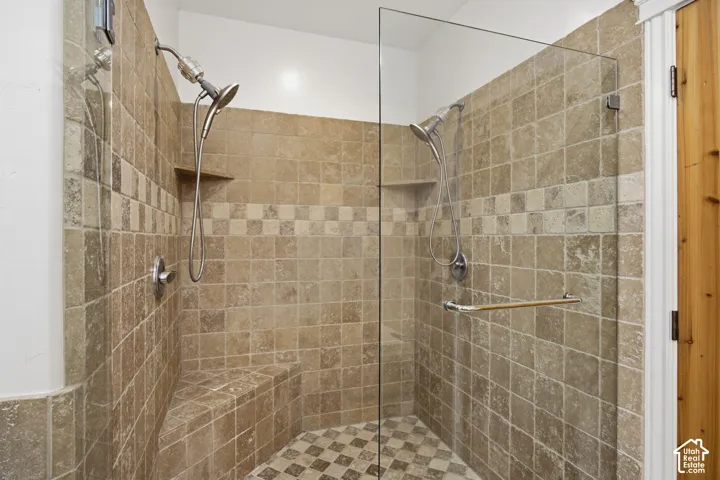 Walk-in shower featuring natural stone tile walls, a built-in corner bench, dual shower heads, and a frameless glass enclosure