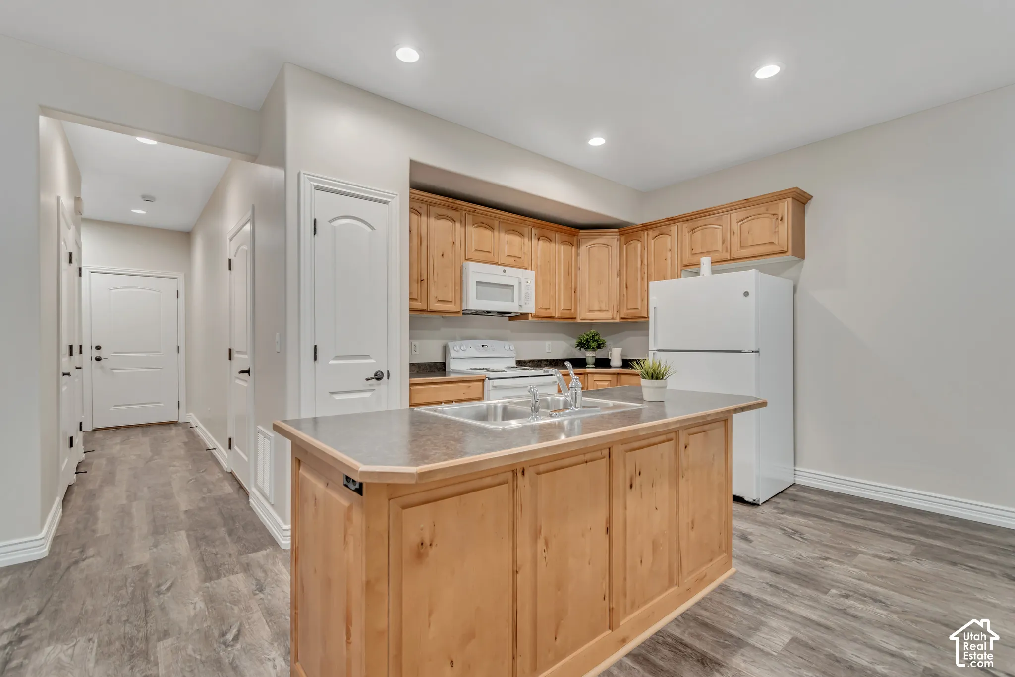 Kitchen featuring wood cabinetry, solid surface countertops, center island with integrated dual-basin sink, recessed lighting, and wood-finish flooring