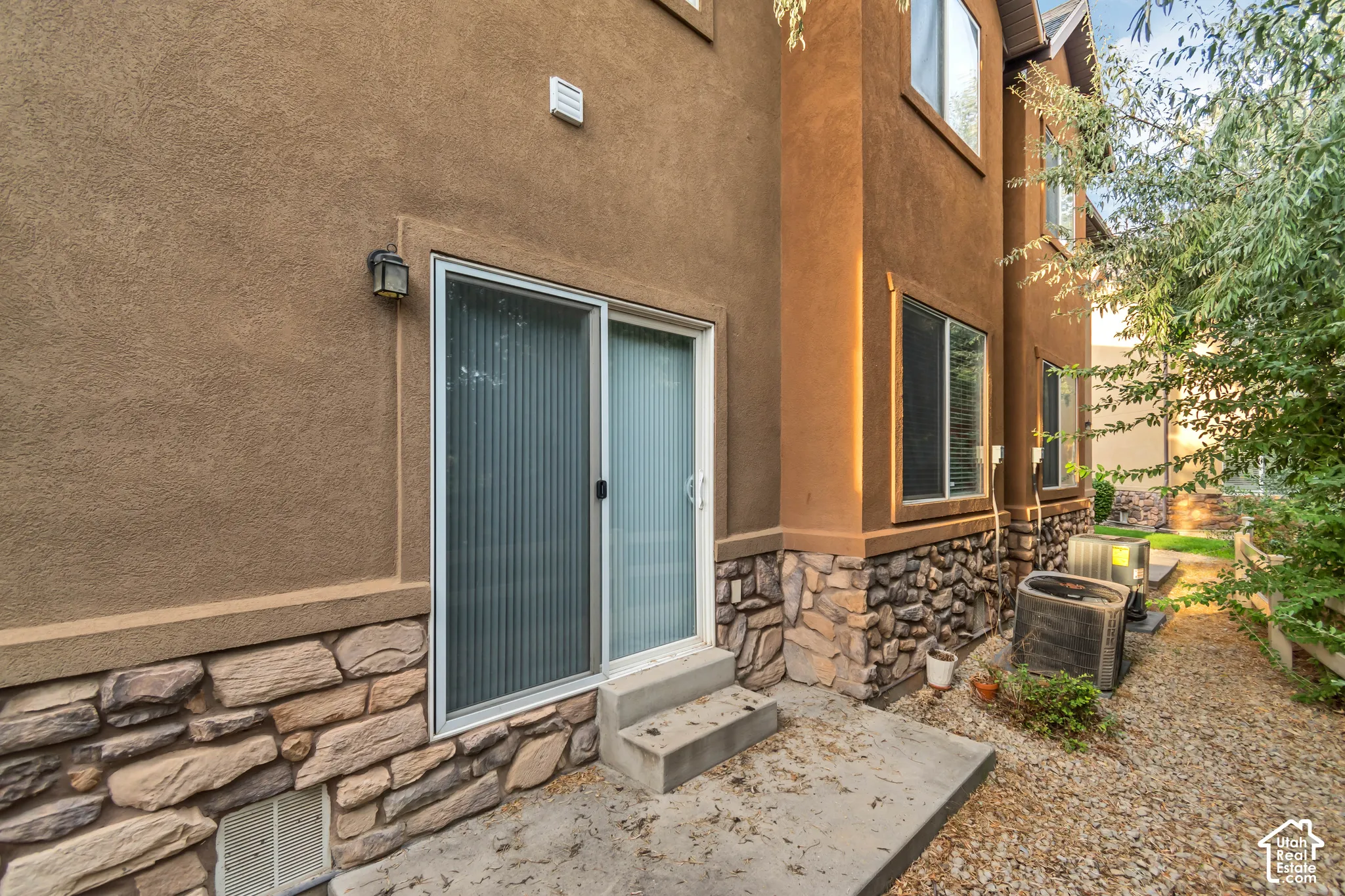 Stucco exterior featuring stone veneer siding, concrete patio, and sliding glass door