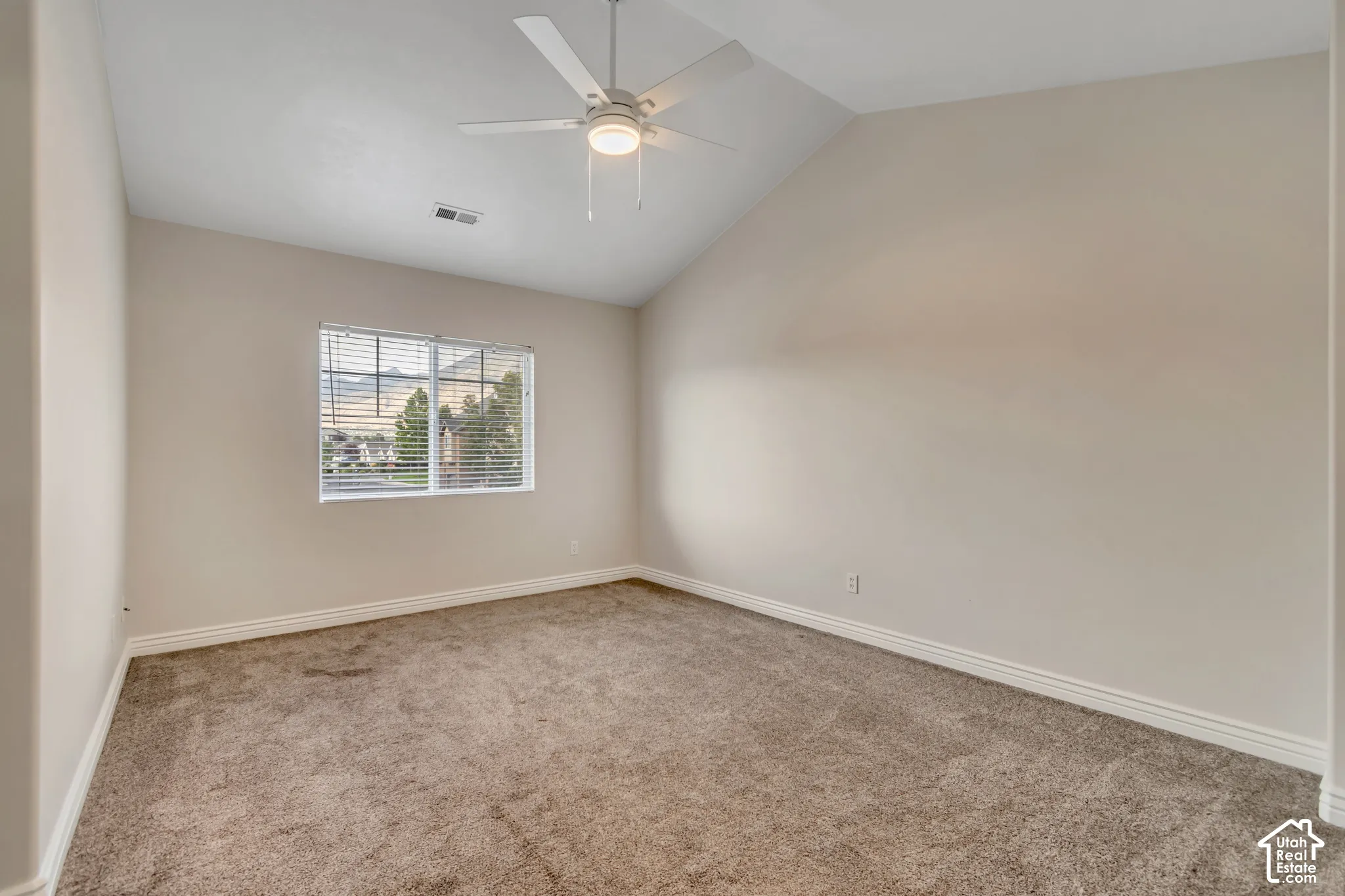 Vaulted ceiling, neutral wall tones, carpeted flooring, and a multi-blade ceiling fan with integrated lighting
