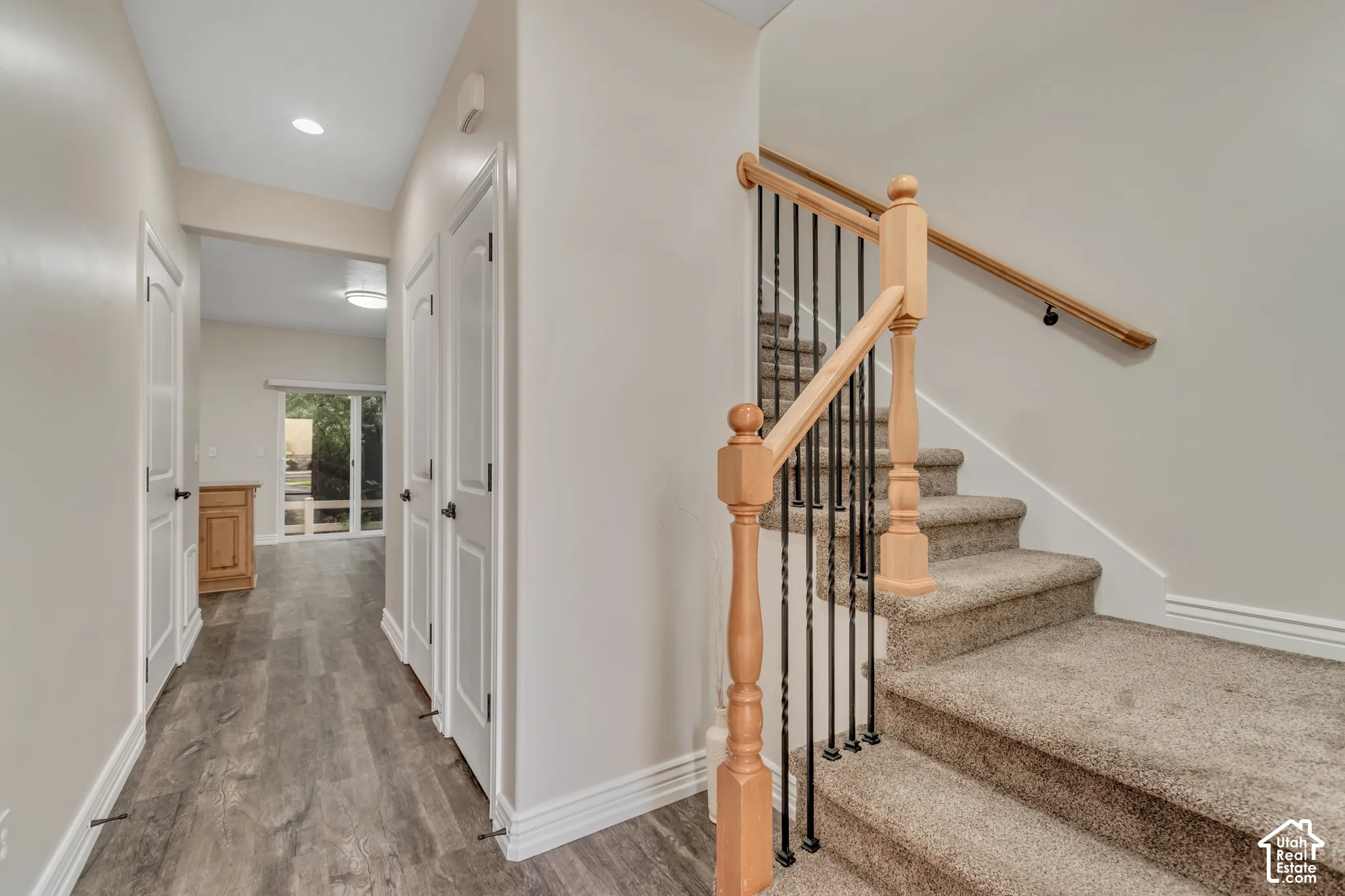 Staircase featuring a natural wood handrail, ornamental wood newel posts, and vertical metal balusters with neutral-toned carpeting