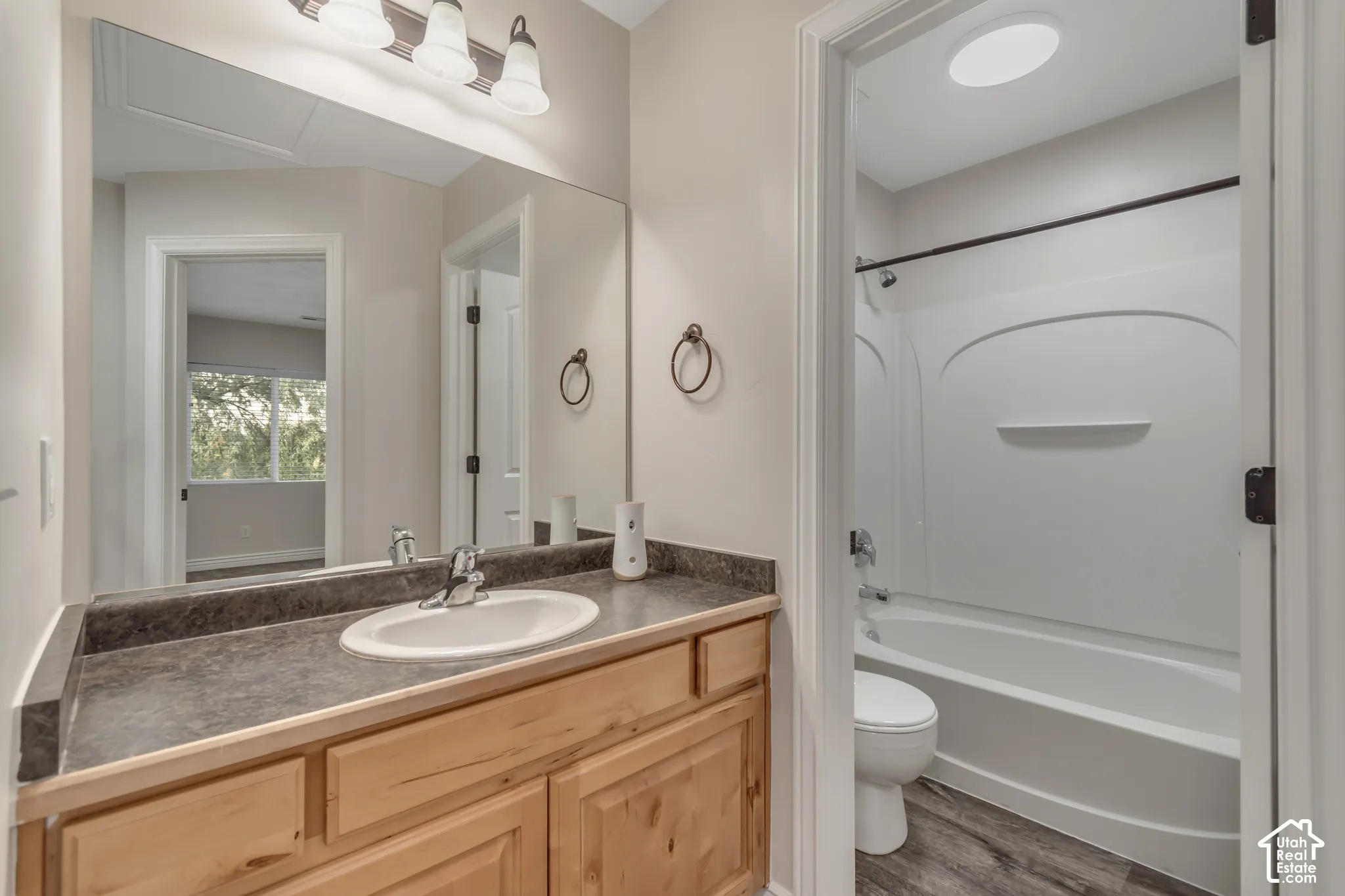 Bathroom featuring a wood-finish vanity with a stone-composite countertop, integrated oval sink, full-width mirror, and a combination tub and shower with a molded surround