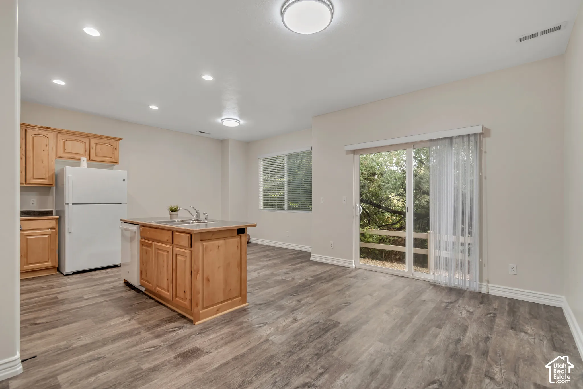 Kitchen area featuring wood-finish cabinetry, a center island with an integrated sink, wood-finish flooring, recessed lighting, and sliding glass doors