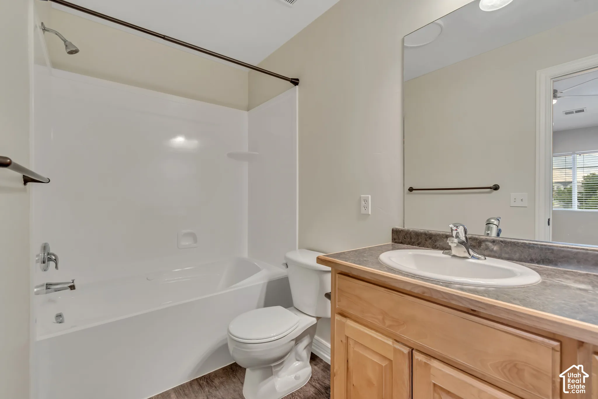Bathroom featuring a wood vanity with a solid surface countertop, an oval under-mount sink, a full-width wall mirror, and a tub-shower combination with a white surround