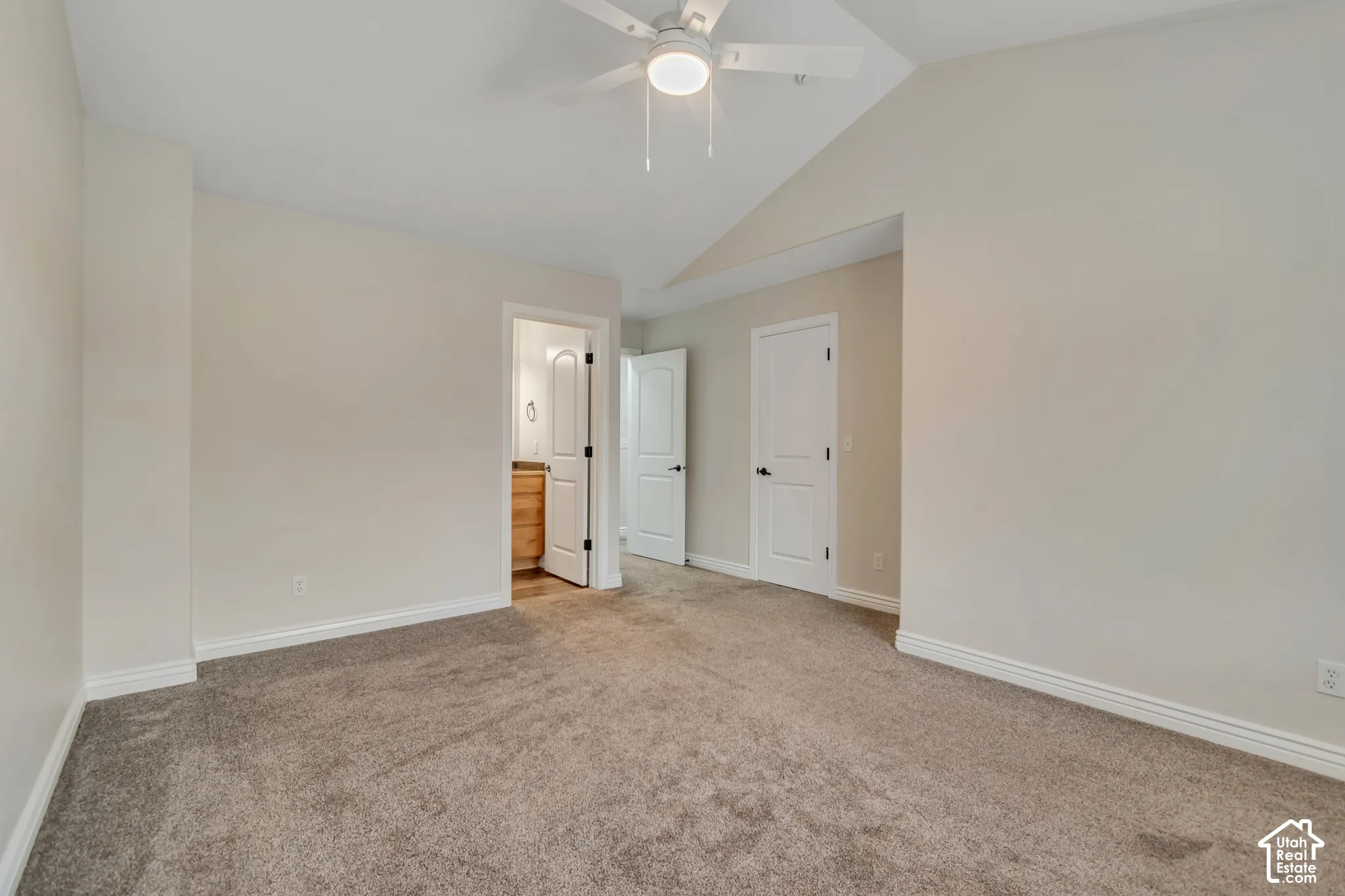 Room featuring a vaulted ceiling, neutral wall tones, carpeted flooring, and a ceiling-mounted light fixture with fan blades