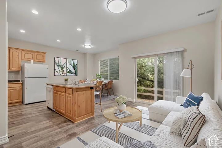 Open-concept kitchen featuring wood-finish cabinetry, a central island with an integrated sink, recessed lighting, and sliding glass doors
