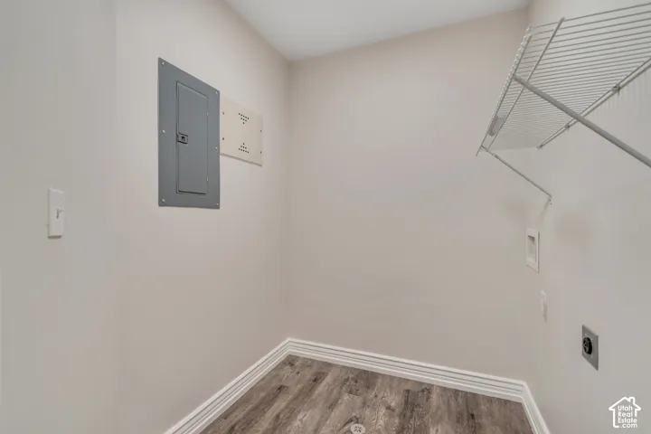 Utility area featuring wood-finish flooring, white wall-mounted wire shelving, and an electrical service panel