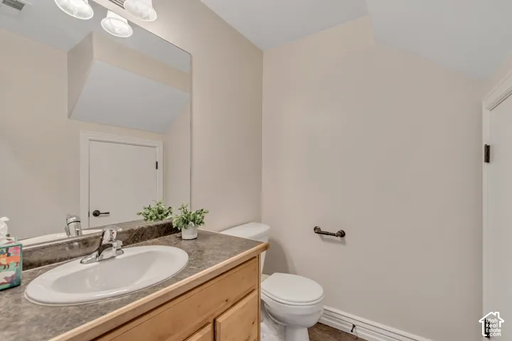 Bathroom featuring a wood-finish vanity with a stone-composite countertop, integrated oval sink, full-width mirror, and three-light overhead fixture