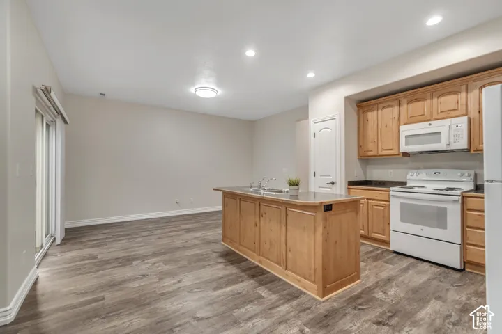 Kitchen featuring wood cabinetry, central island with a double basin sink, wood-finish flooring, and recessed lighting