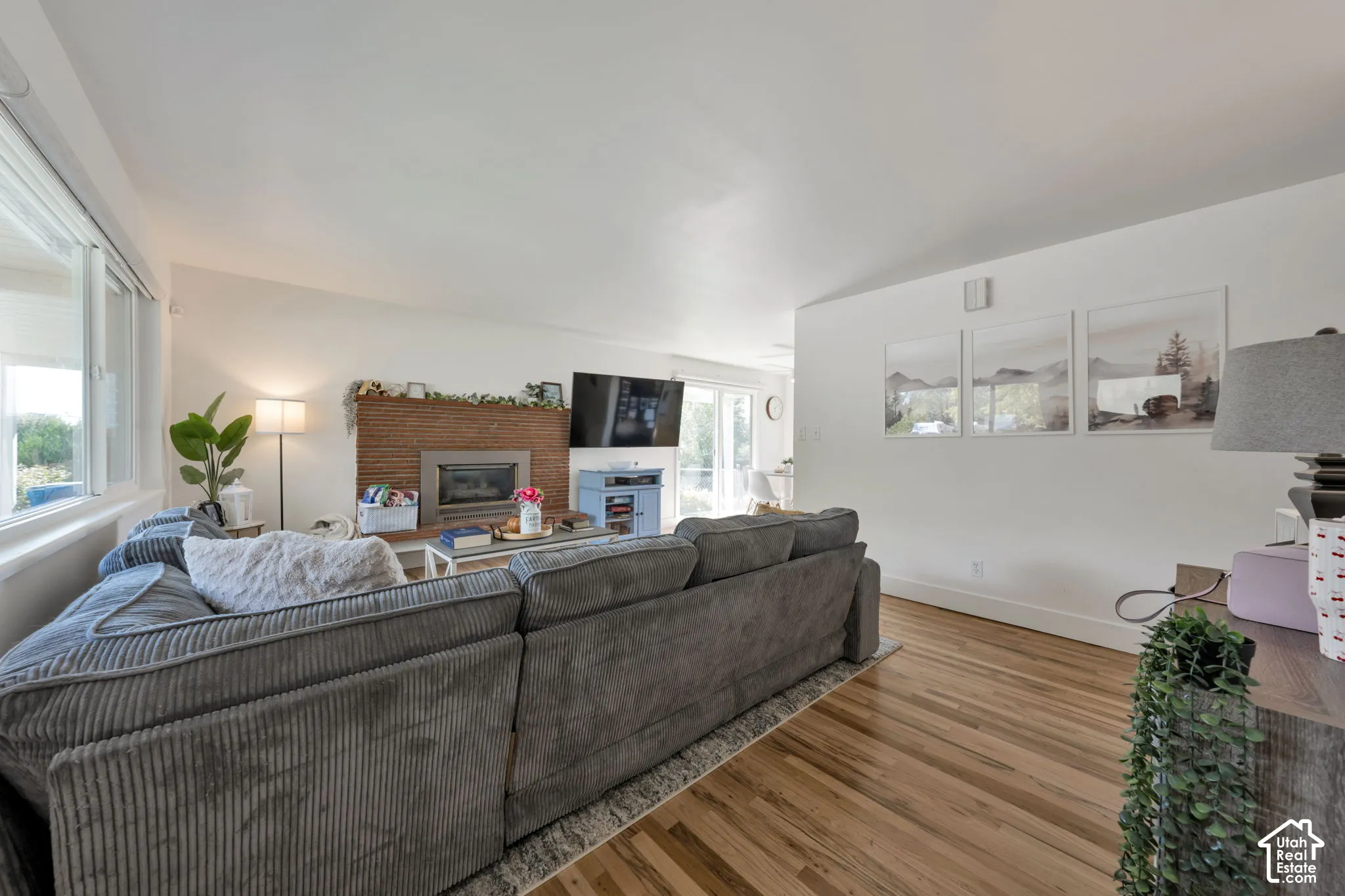 Living area featuring wood-finish flooring, a textured stone-surround fireplace, and large windows