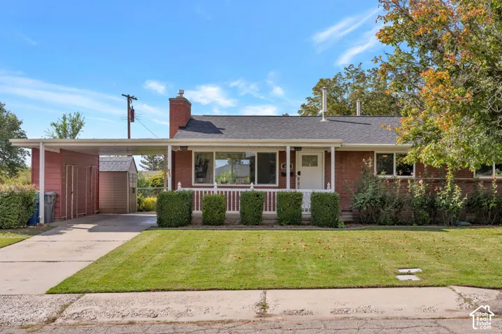Brick exterior featuring a covered carport, front porch with white railing, and a brick chimney