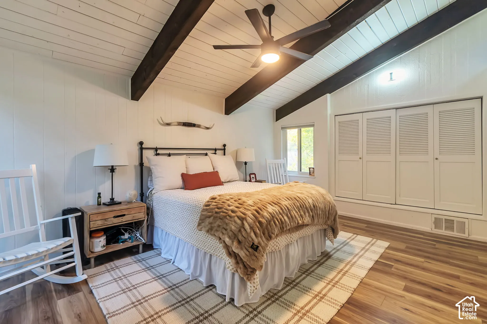 Bedroom 1 with vaulted ceiling with exposed wooden beams, wood-finish flooring, and built-in louvered-panel closets