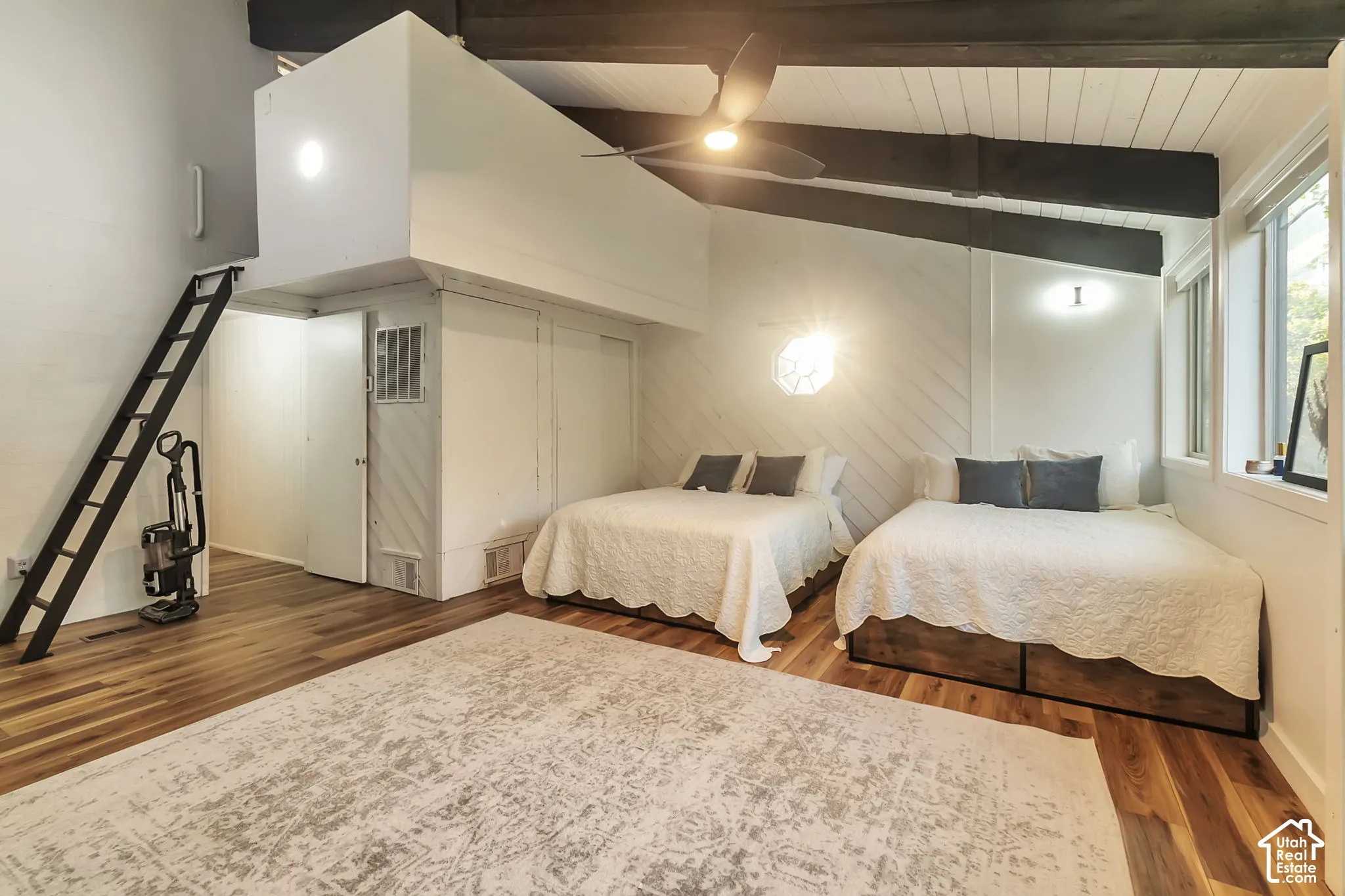 Vaulted ceiling featuring exposed dark-finish beams and white tongue-and-groove paneling, wood-finish flooring, and a fixed metal ladder