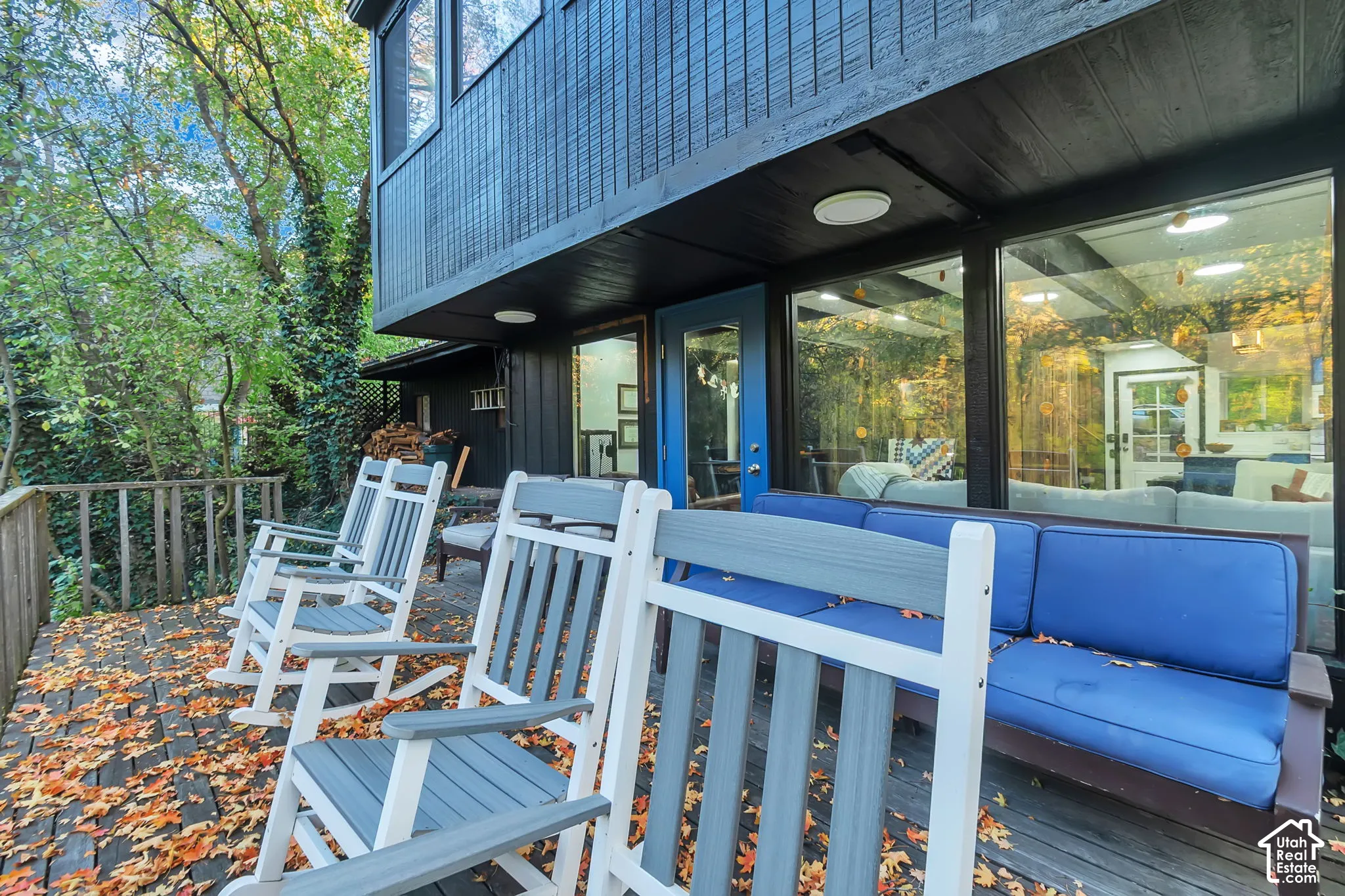 Wood-deck terrace featuring black exterior wood siding, expansive floor-to-ceiling glass windows, and a blue painted entry door