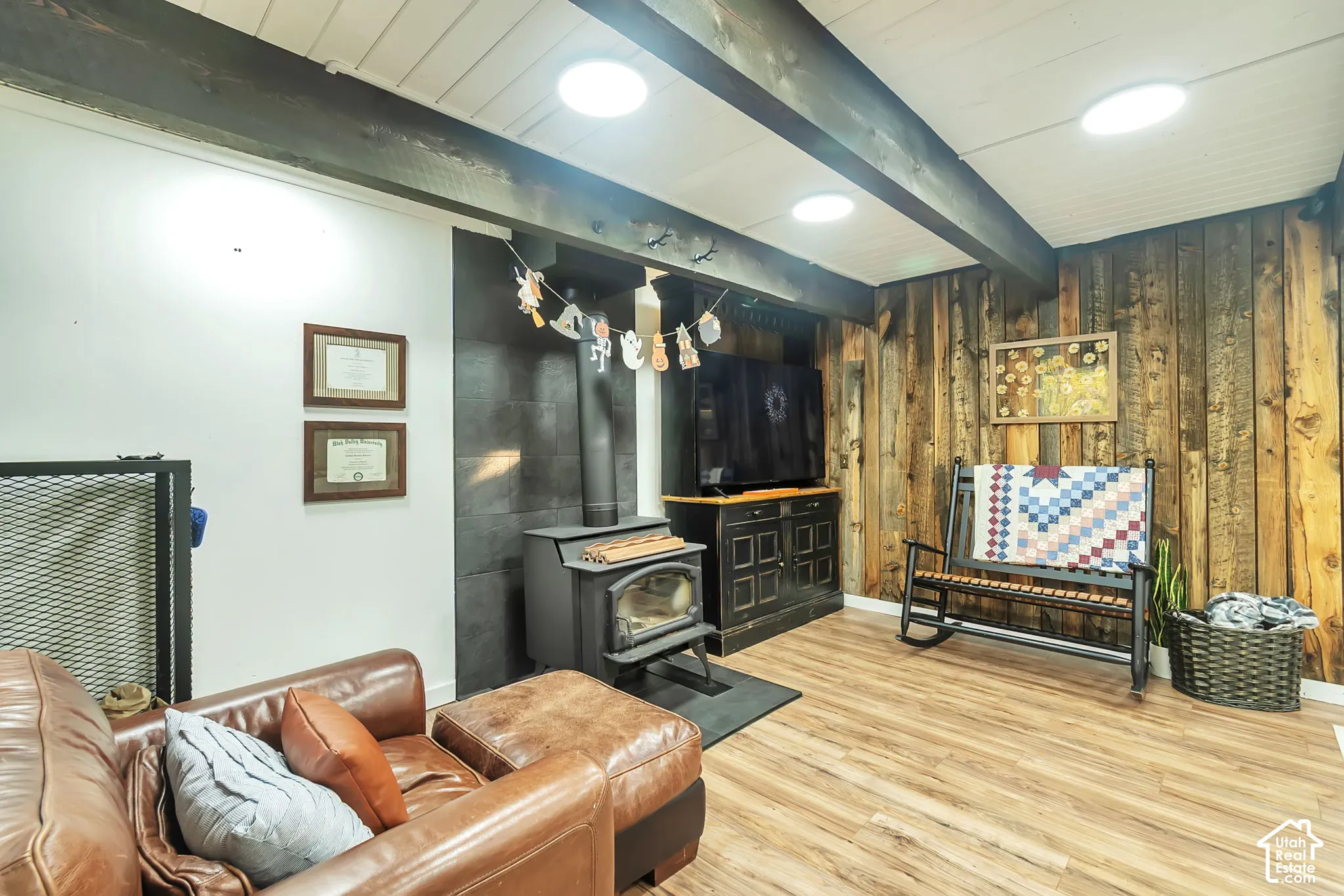 Wood-finish flooring, exposed ceiling beams, vertical wood-plank wall cladding, and a freestanding wood-burning stove with a tile surround