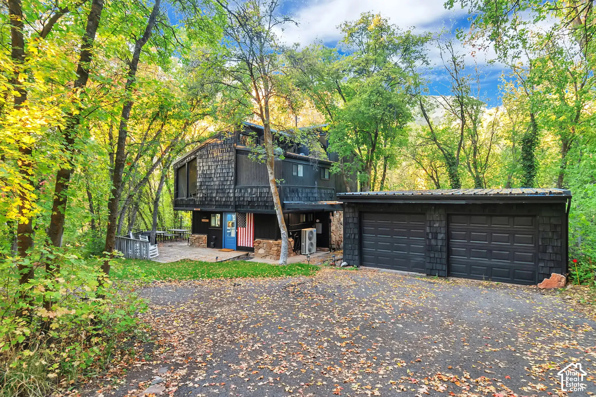 Multi-level exterior featuring dark wood shake siding, stone foundation detailing, an attached two-car garage with a metal roof, and an expansive paved outdoor space