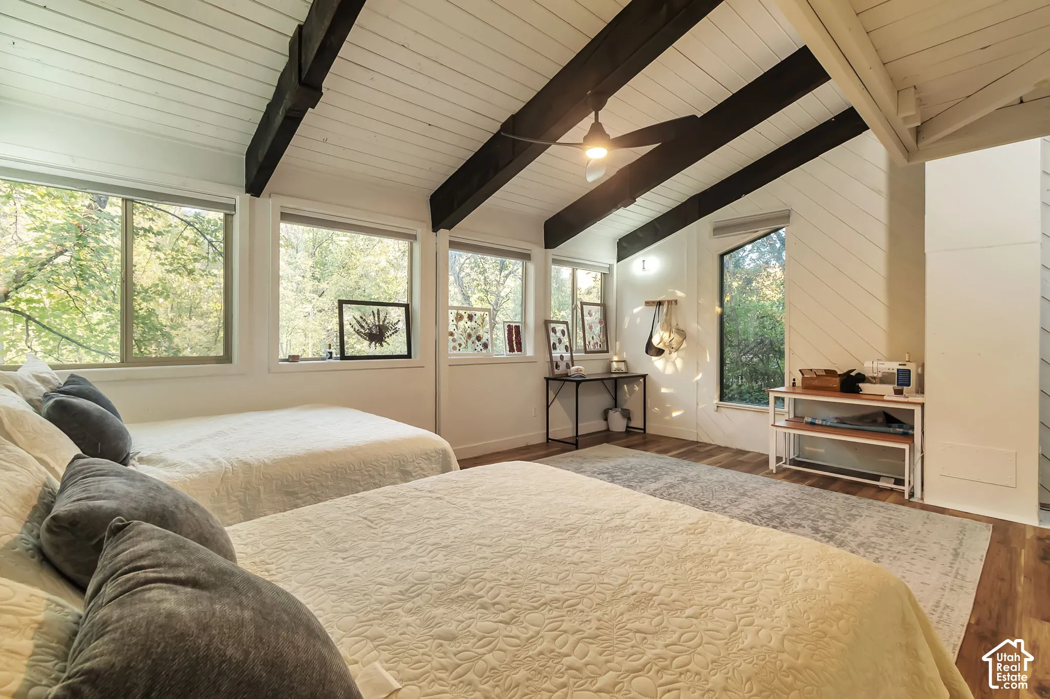 Large 2nd bedroom with vaulted ceiling with exposed decorative beams, tongue-and-groove plank ceiling, wood-finish flooring, multi-pane windows, and diagonal wall paneling