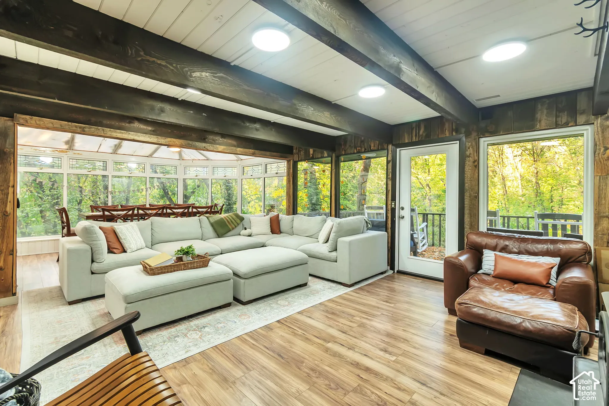 Wood-finish flooring, exposed stained wood ceiling beams, white planked ceiling, expansive windows, and glass-paneled exterior door