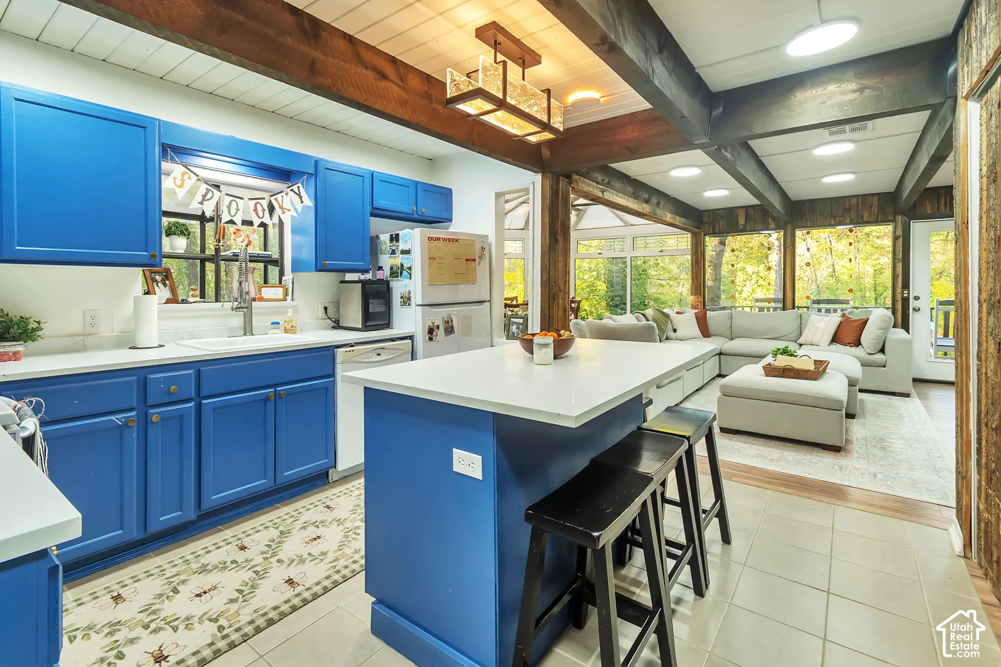 Kitchen featuring a central island with a solid surface countertop, blue cabinetry, exposed wooden ceiling beams, and a geometric pendant light fixture