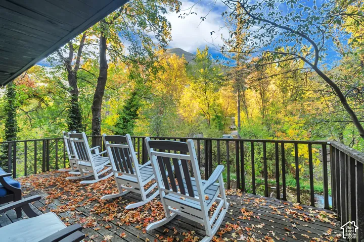 Elevated wooden deck featuring a perimeter railing and mature deciduous trees set against a mountain backdrop