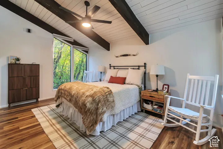 Vaulted ceilings featuring exposed dark-finish structural beams, wood-finish flooring, and large multi-pane windows