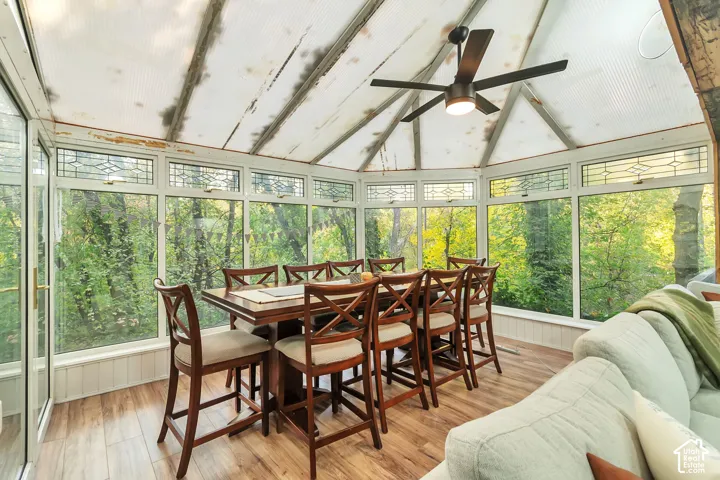 Sunroom featuring a vaulted semi-translucent roof, wood-finish flooring, extensive glass-paneled walls, and an integrated ceiling fan