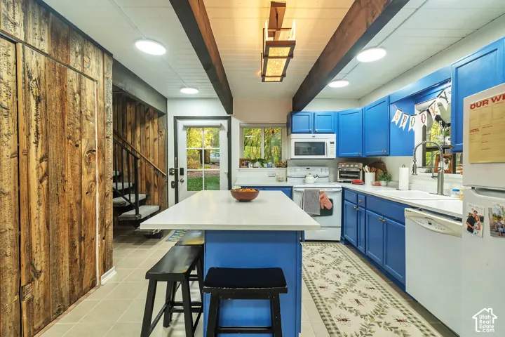 Kitchen featuring exposed timber ceiling beams, wood-plank wall paneling, a central island with a quartz countertop, and custom blue cabinetry